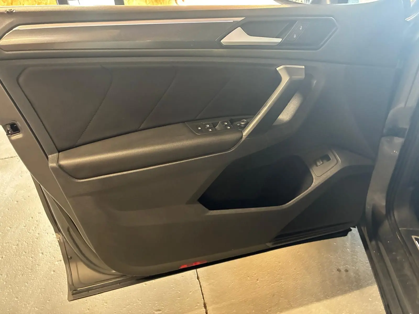 Vue intérieure côté gauche de la porte avant d’un Volkswagen Tiguan gris, avec commandes électriques et garniture noire.