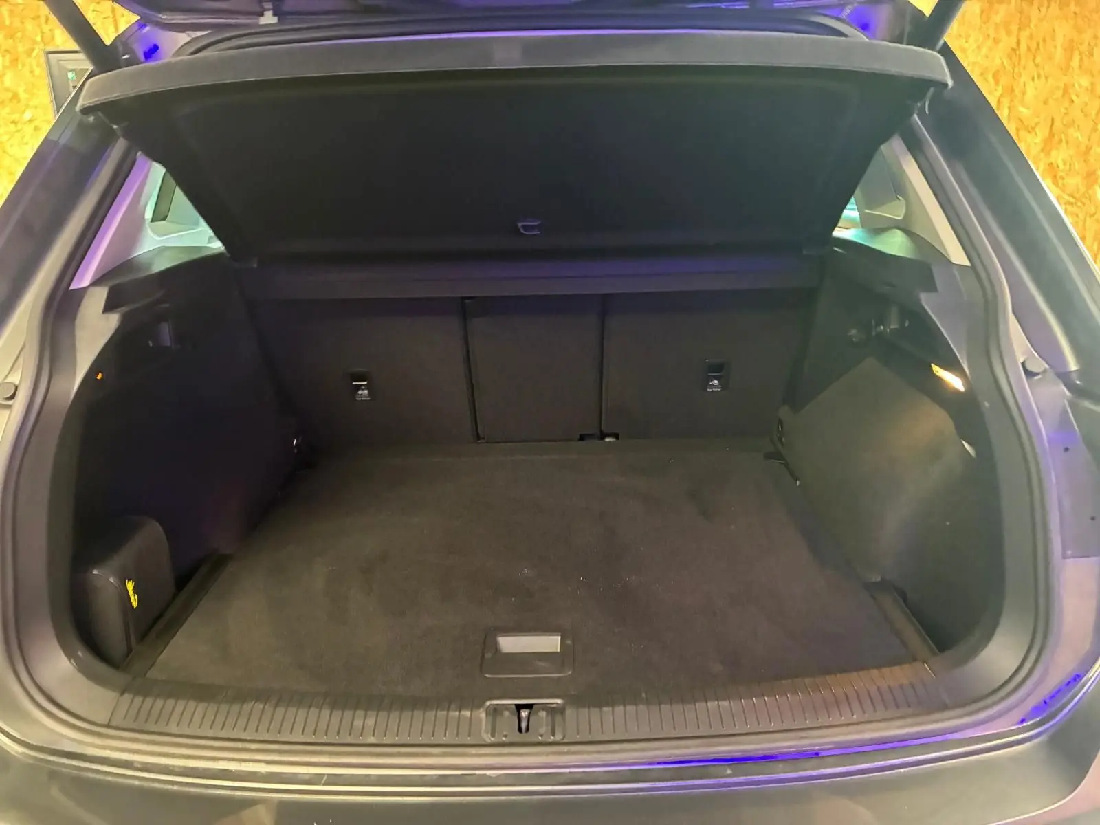 Coffre ouvert d’un Volkswagen Tiguan gris, vue arrière montrant l’espace de chargement vide et la tablette cache-bagages relevée.