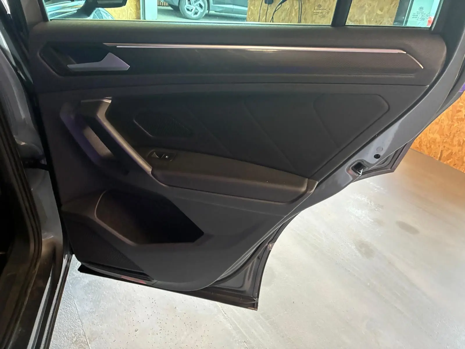 Vue intérieure de la porte arrière gauche gris foncé du Volkswagen Tiguan 2020 avec poignée et commande de fenêtre intégrées.