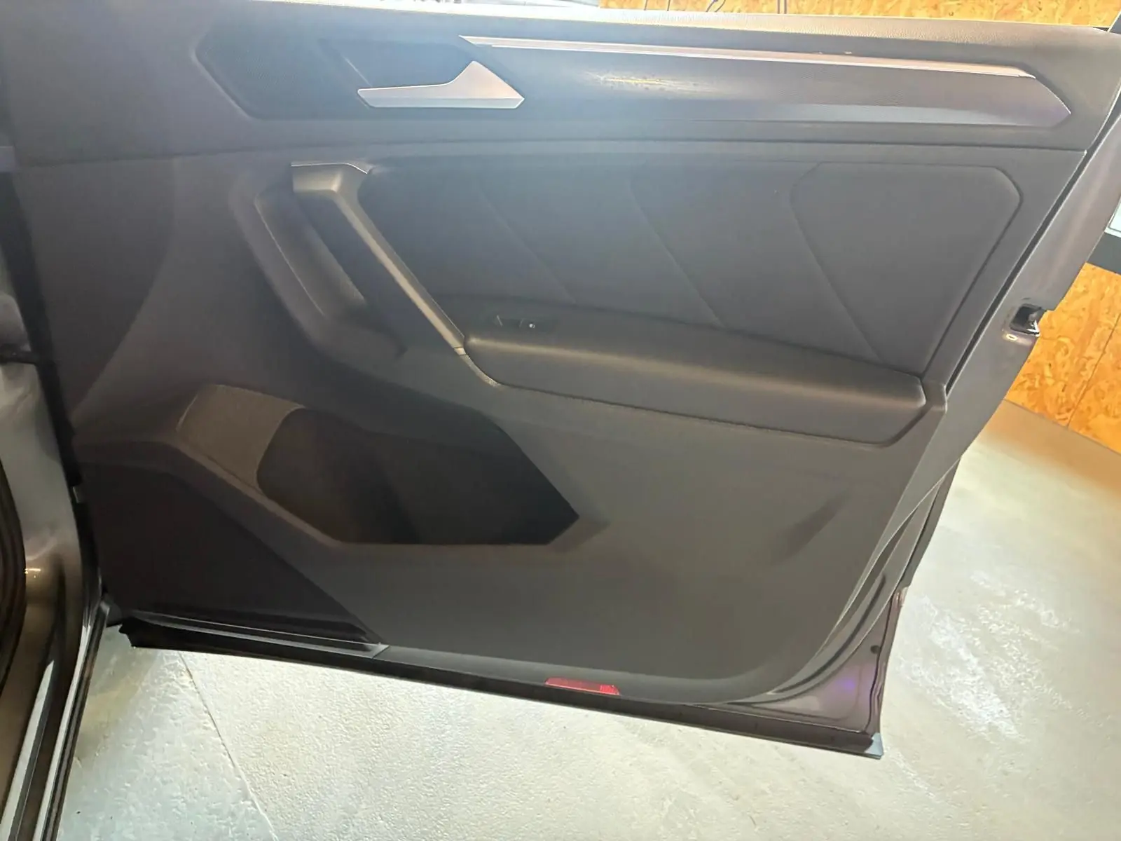 Vue intérieure du panneau de porte côté gauche du Volkswagen Tiguan gris, avec garniture noire et poignée intégrée.