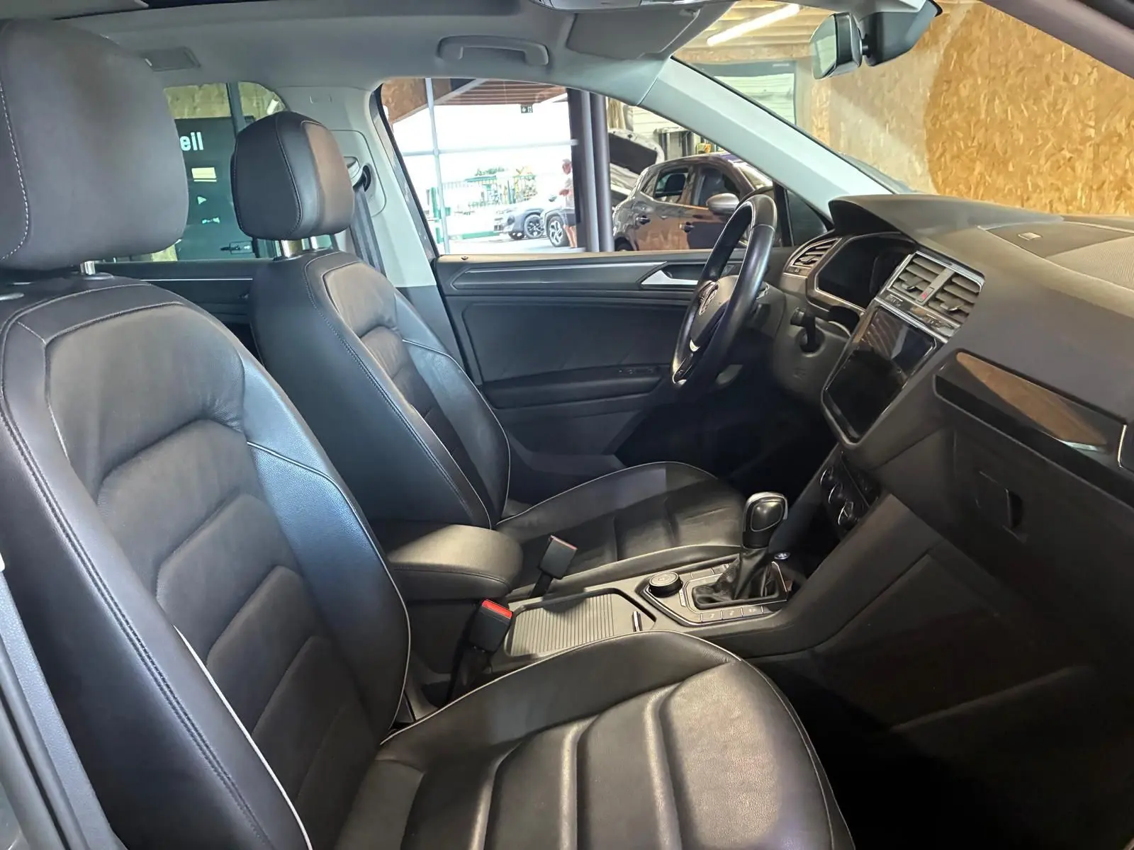 Vue intérieure côté conducteur du Volkswagen Tiguan 2.0 TDI gris, sièges cuir noir et console centrale avec boîte auto.