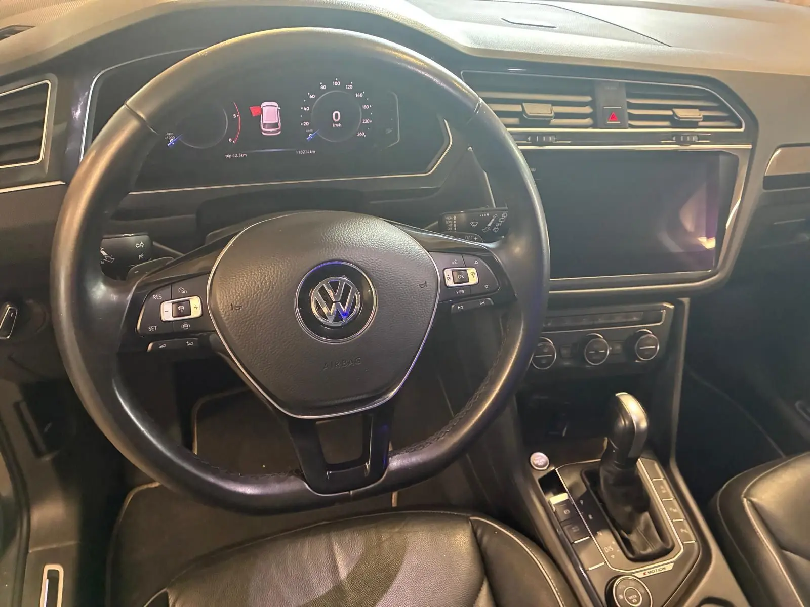 Vue intérieure centrée sur le volant noir et la console centrale d'un Volkswagen Tiguan gris, avec écran tactile éteint.