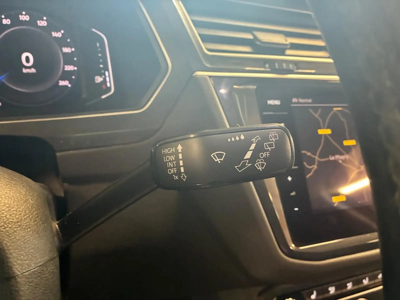 Gros plan sur la commande d’essuie-glace à gauche du volant dans l’habitacle noir du Volkswagen Tiguan gris, avec tableau de bord digital et écran GPS.