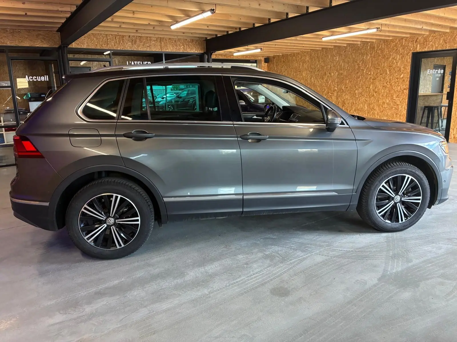 Vue de profil côté gauche d'un Volkswagen Tiguan gris 2020 garé en intérieur avec jantes alliage noires et chrome.
