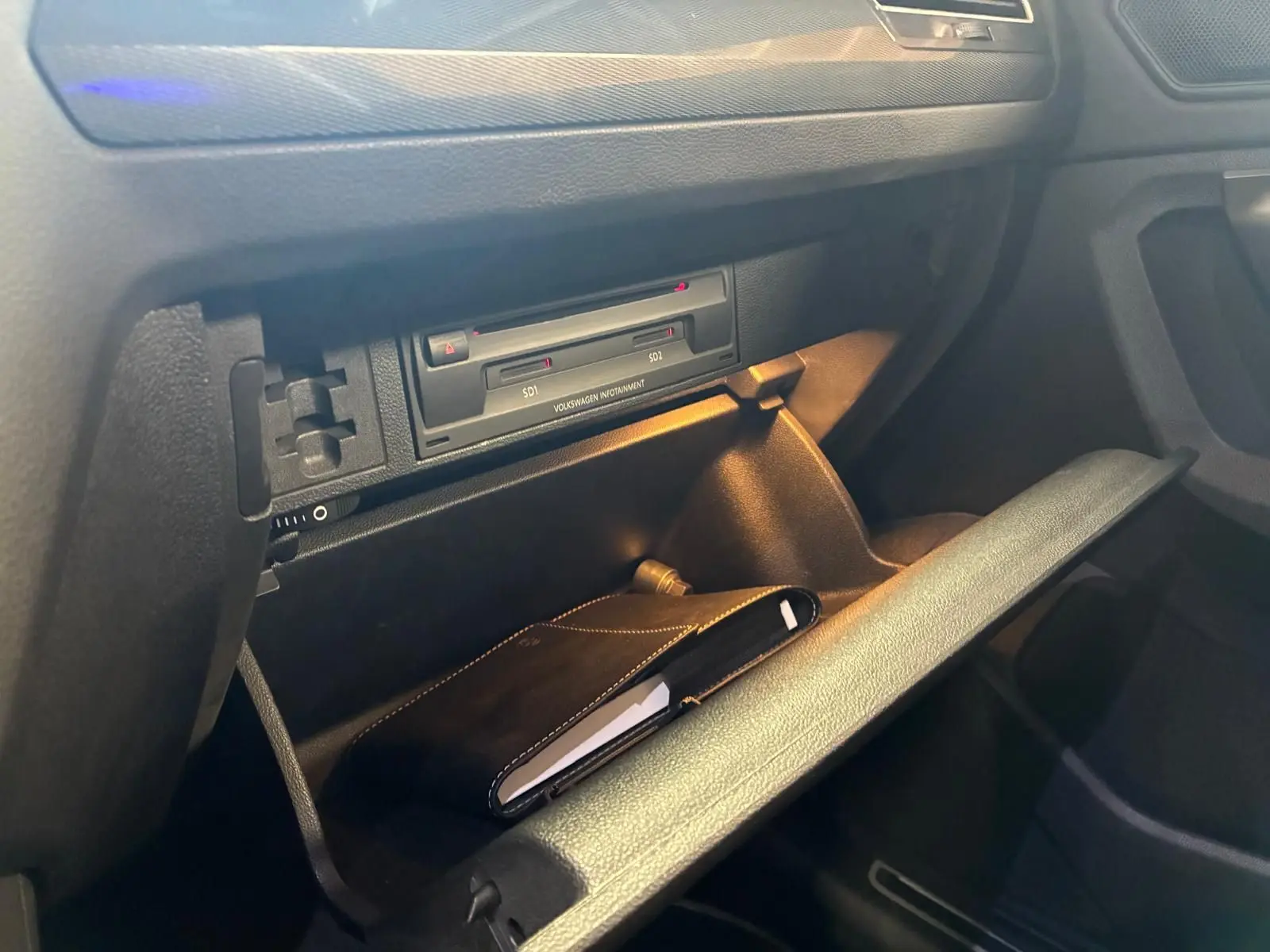 Gros plan sur la boîte à gants ouverte du Volkswagen Tiguan gris 2020, avec un carnet noir à l'intérieur.