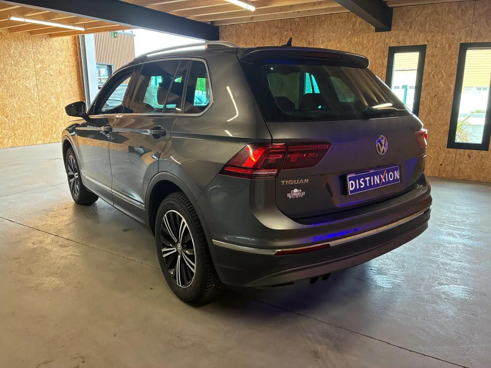 Vue 3/4 arrière droite d'un Volkswagen Tiguan gris stationné en intérieur avec feux arrière allumés et jantes noires.