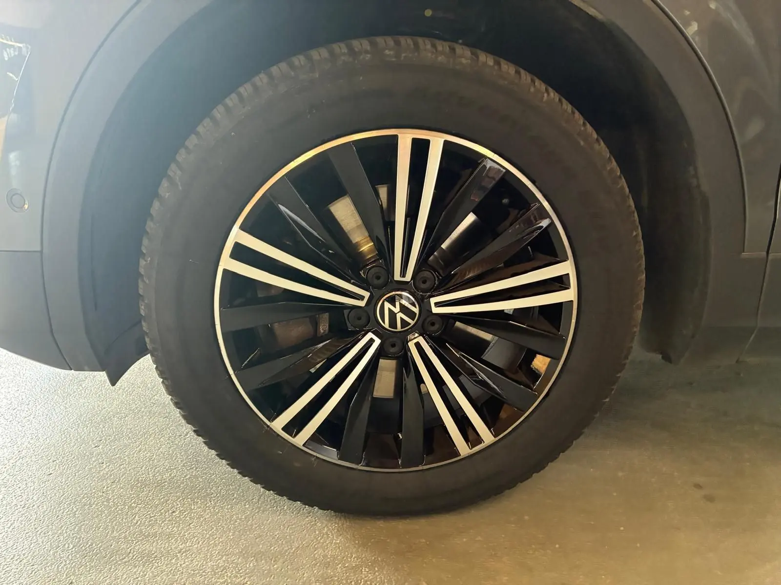 Gros plan sur la roue avant gauche d’un Volkswagen Tiguan gris, mettant en valeur la jante noire et argentée au design moderne.