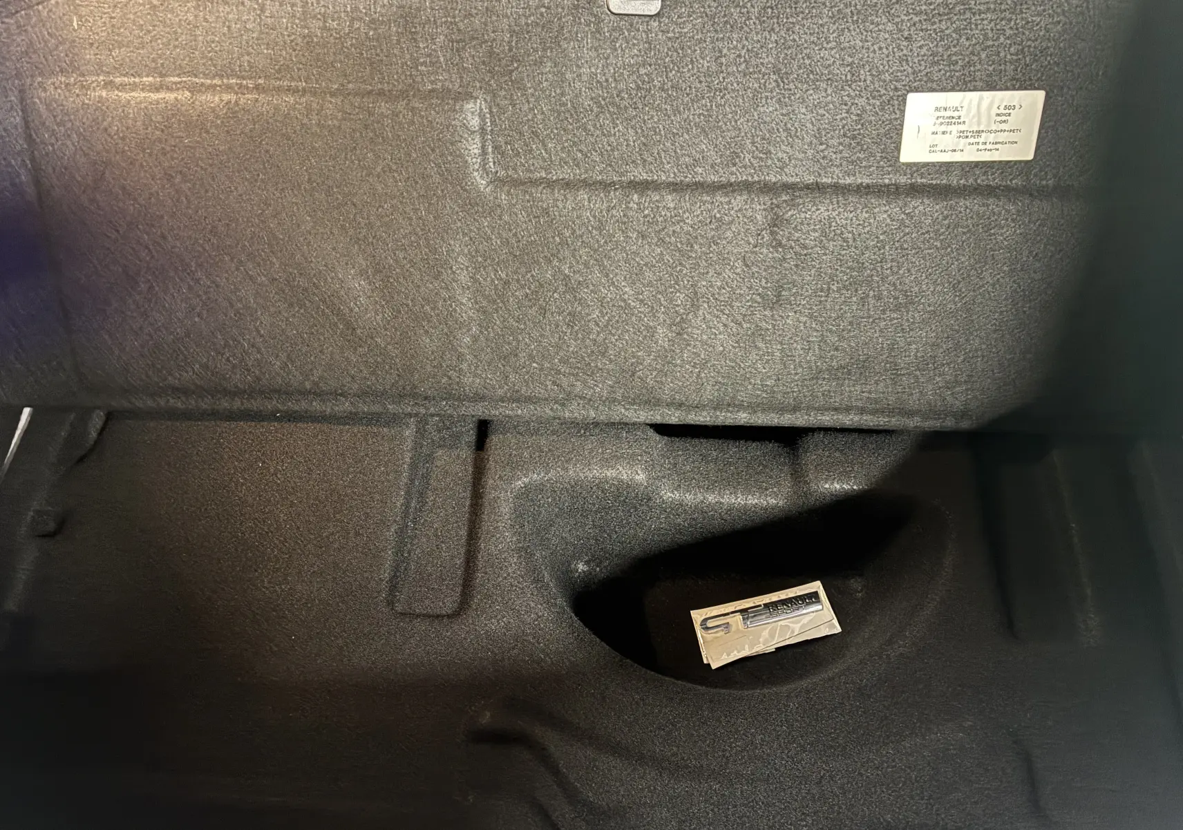 Vue rapprochée de l'intérieur du coffre noir d'une Renault Mégane Coupé blanc, badge GT visible au fond.
