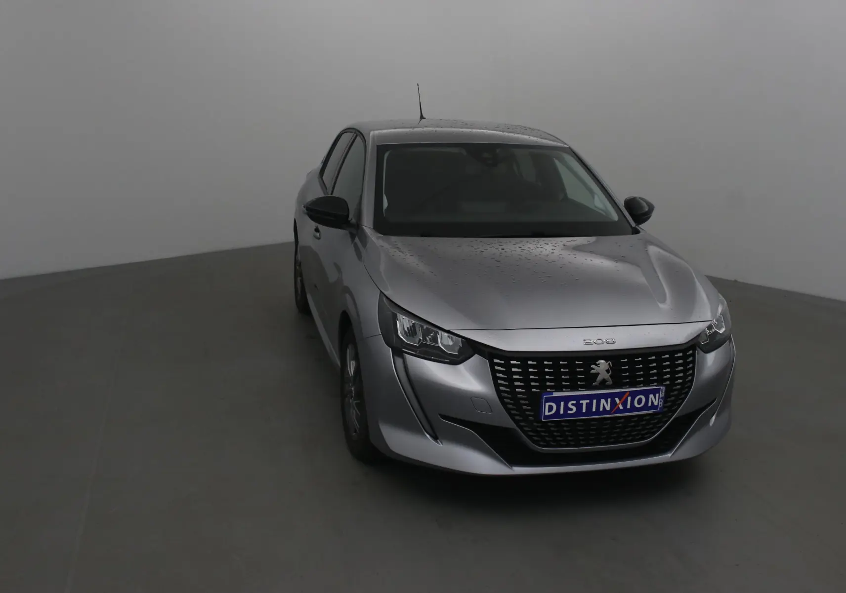 Peugeot 208 1.2 PureTech 100 Style gris Artense vue 3/4 avant avec calandre distinctive et pluie sur la carrosserie.