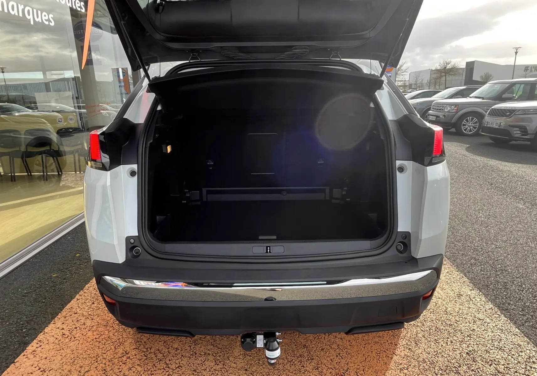 Vue arrière d’un Peugeot 3008 blanc 2018 avec coffre ouvert et attelage visible au centre.