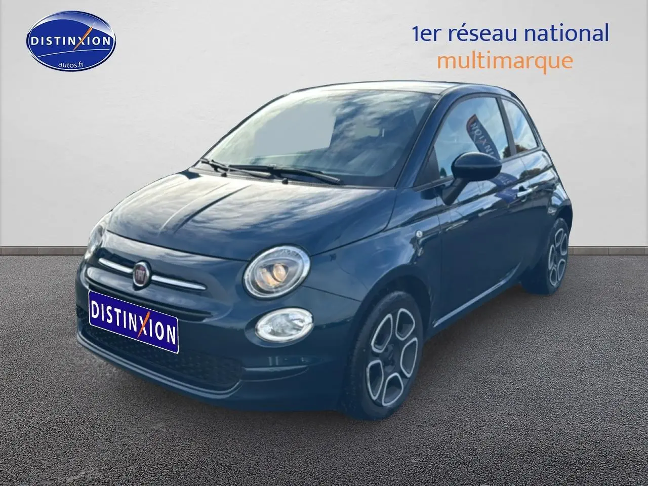 Vue 3/4 avant droite d'une FIAT 500 bleu foncé avec phares allumés sur fond neutre.