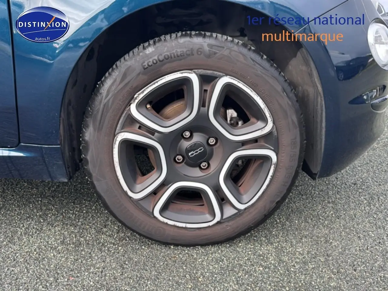 Gros plan sur la roue avant gauche d'une FIAT 500 bleu foncé avec jante spécifique et logo central visible.