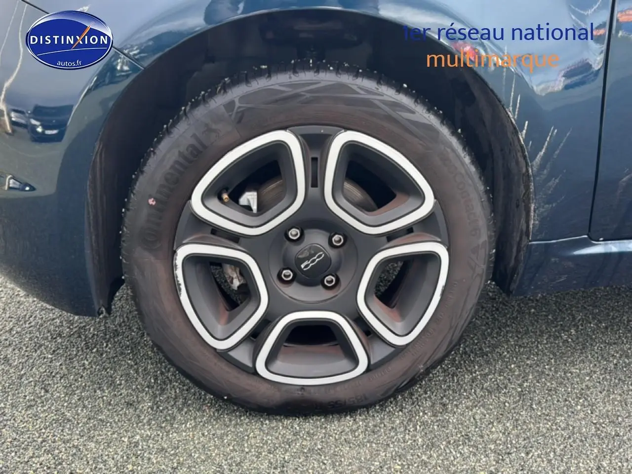 Gros plan sur la roue avant droite d'une FIAT 500 bleu foncé, avec jante noire et argentée au design distinctif.