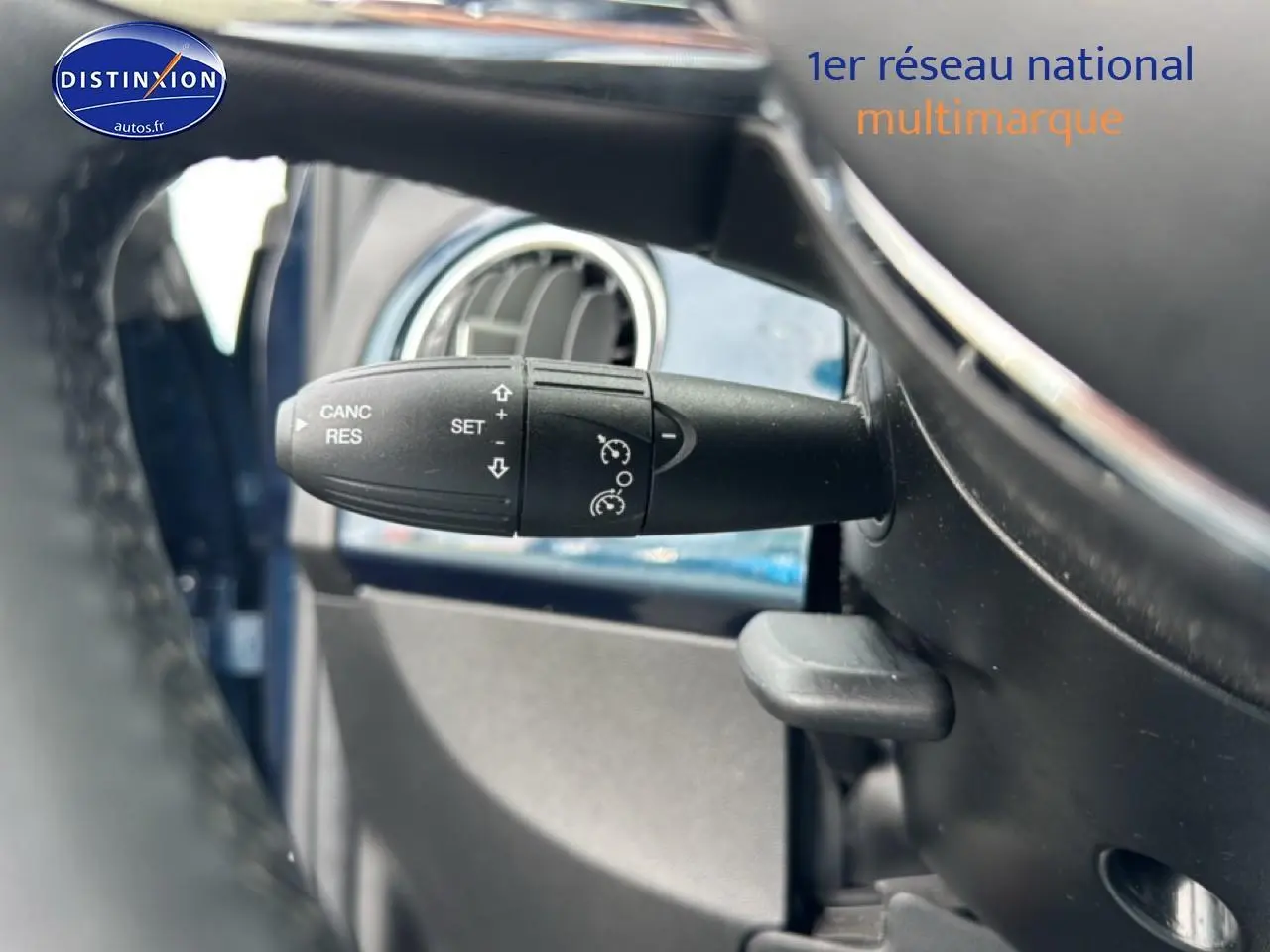 Gros plan sur la commande de régulateur de vitesse à gauche du volant d’une FIAT 500 bleu foncé 2023.