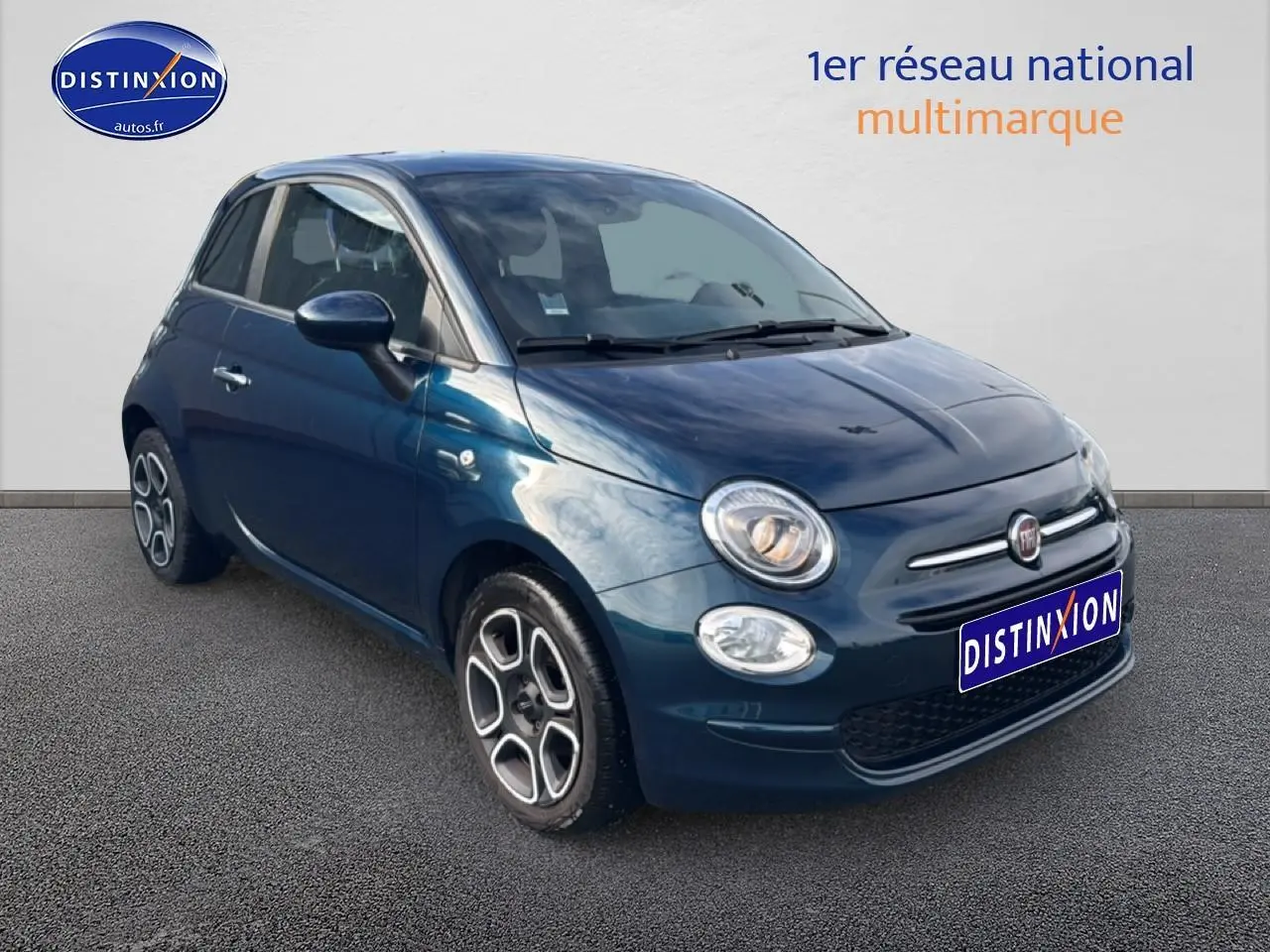 Vue 3/4 avant droite d'une FIAT 500 bleu foncé 2023 avec jantes stylisées et phares allumés.