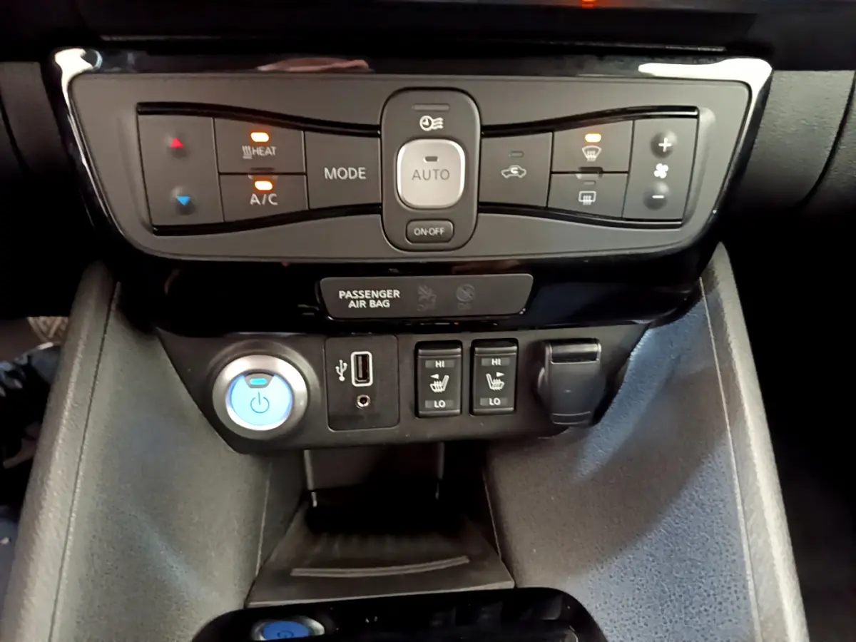 Vue rapprochée du tableau de bord central de la Nissan Leaf blanche 2020, avec commandes climatisation et sièges chauffants.