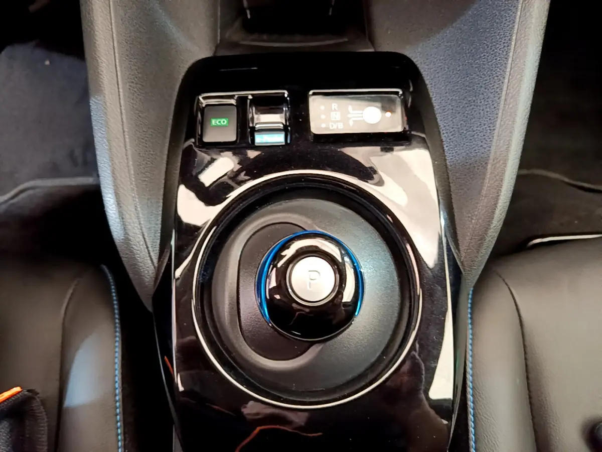 Gros plan sur la molette de boîte automatique noire avec bouton "P" bleu au centre de la console d'une Nissan Leaf blanche.