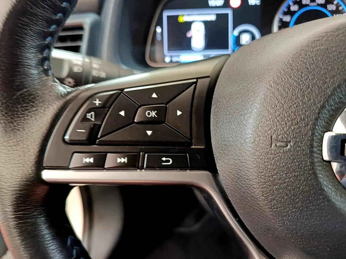 Gros plan sur les commandes gauche du volant cuir de la Nissan LEAF 62 kWh 2020 avec affichage numérique en arrière-plan.