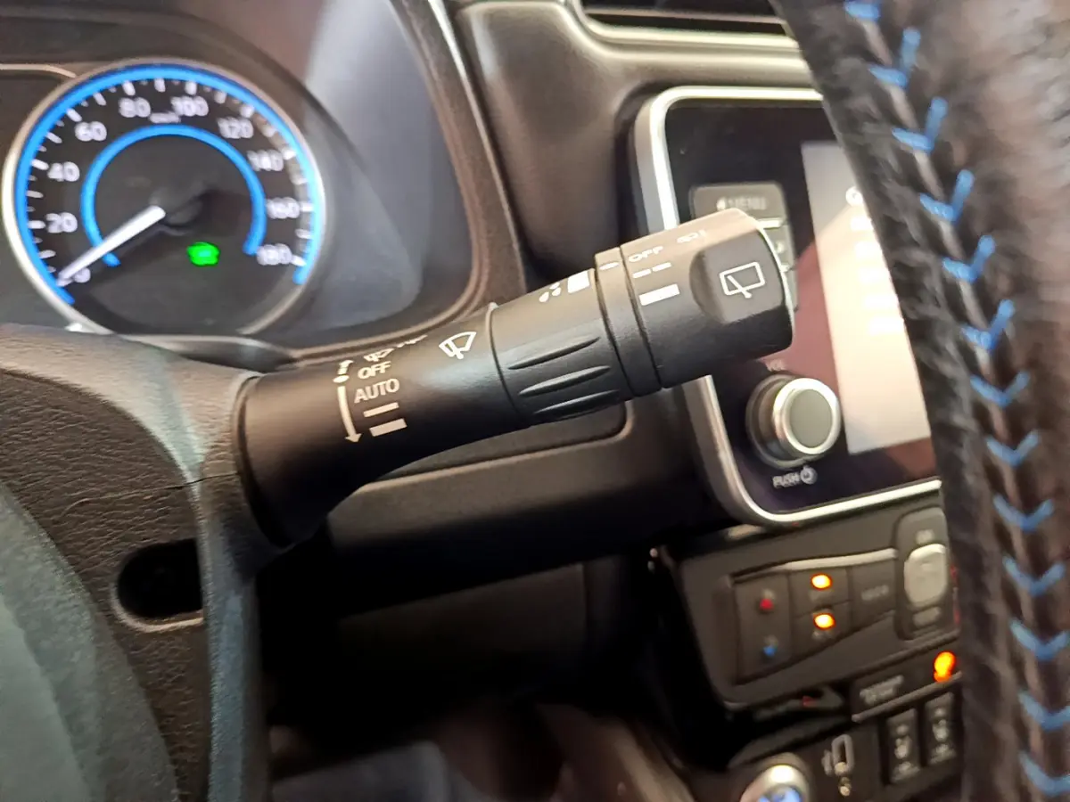 Gros plan sur la commande d’essuie-glace à gauche du volant cuir noir avec surpiqûres bleues du Nissan Leaf blanc 2020.