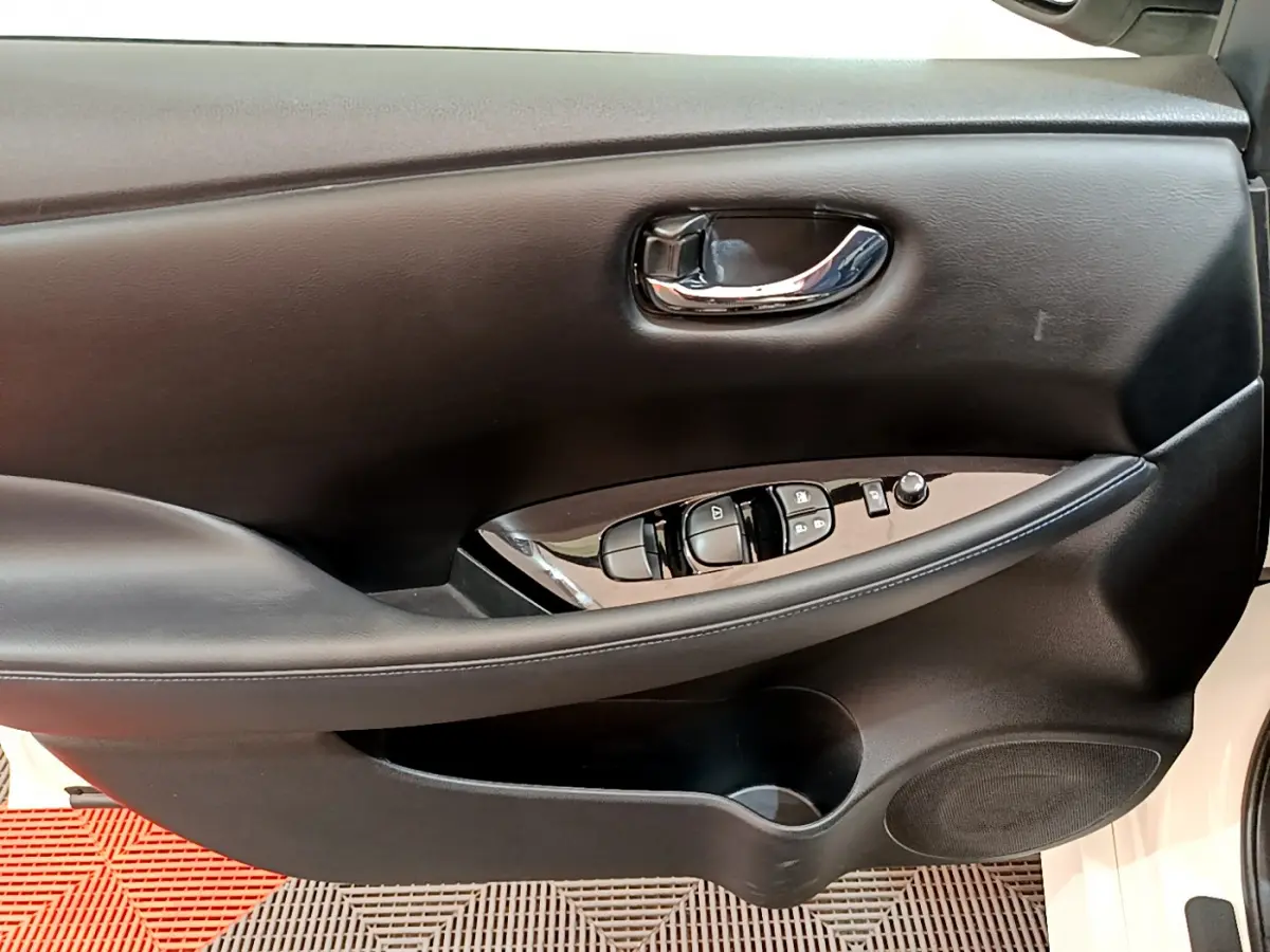 Gros plan sur la porte intérieure côté conducteur noire du Nissan Leaf blanc, avec commandes électriques et poignée chromée.