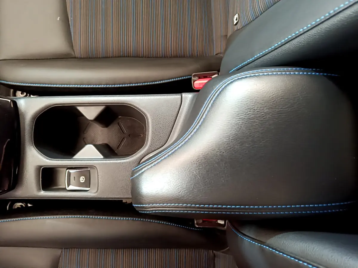 Gros plan sur la console centrale noire avec surpiqûres bleues et porte-gobelet du Nissan Leaf blanc 2020.