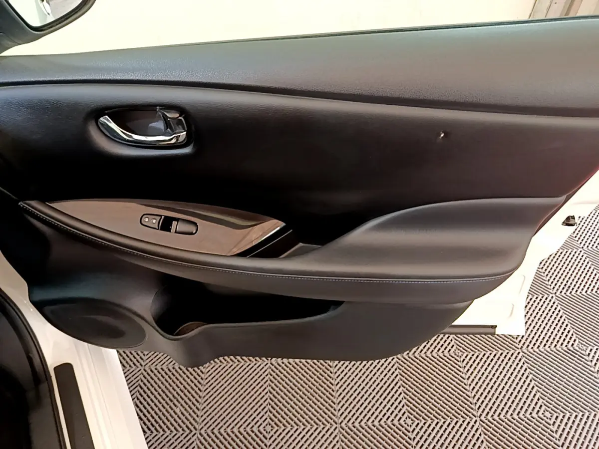 Porte intérieure côté gauche de Nissan Leaf blanche 2020, avec poignée chrome et commandes de vitres noires.