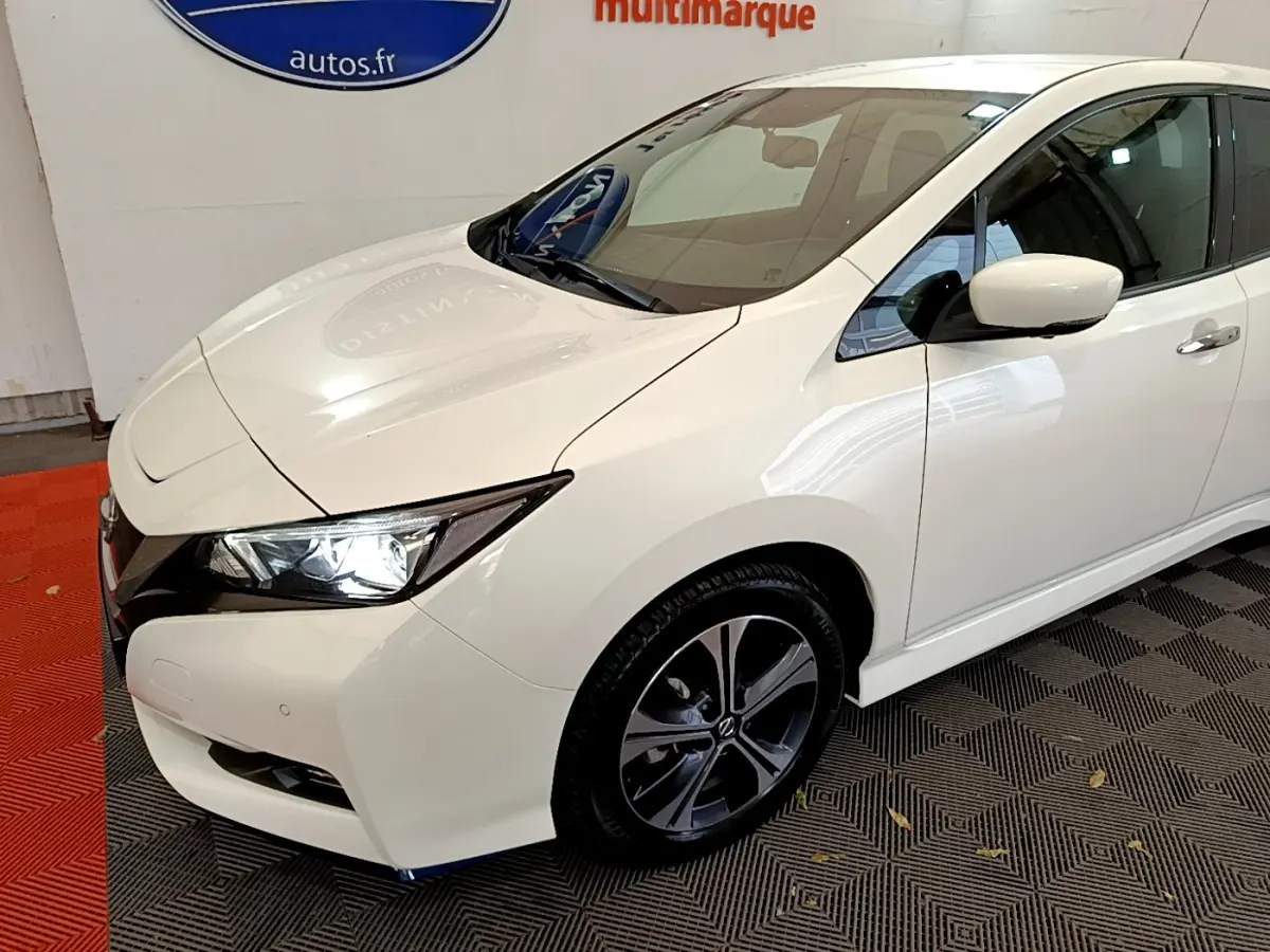 Nissan Leaf blanc vue 3/4 avant droit, phares LED allumés et jantes alliage distinctives.