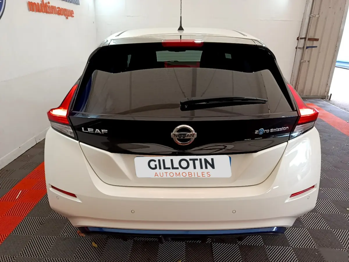 Vue arrière d'une Nissan Leaf blanche avec hayon noir brillant et feux arrière LED allumés dans un garage.