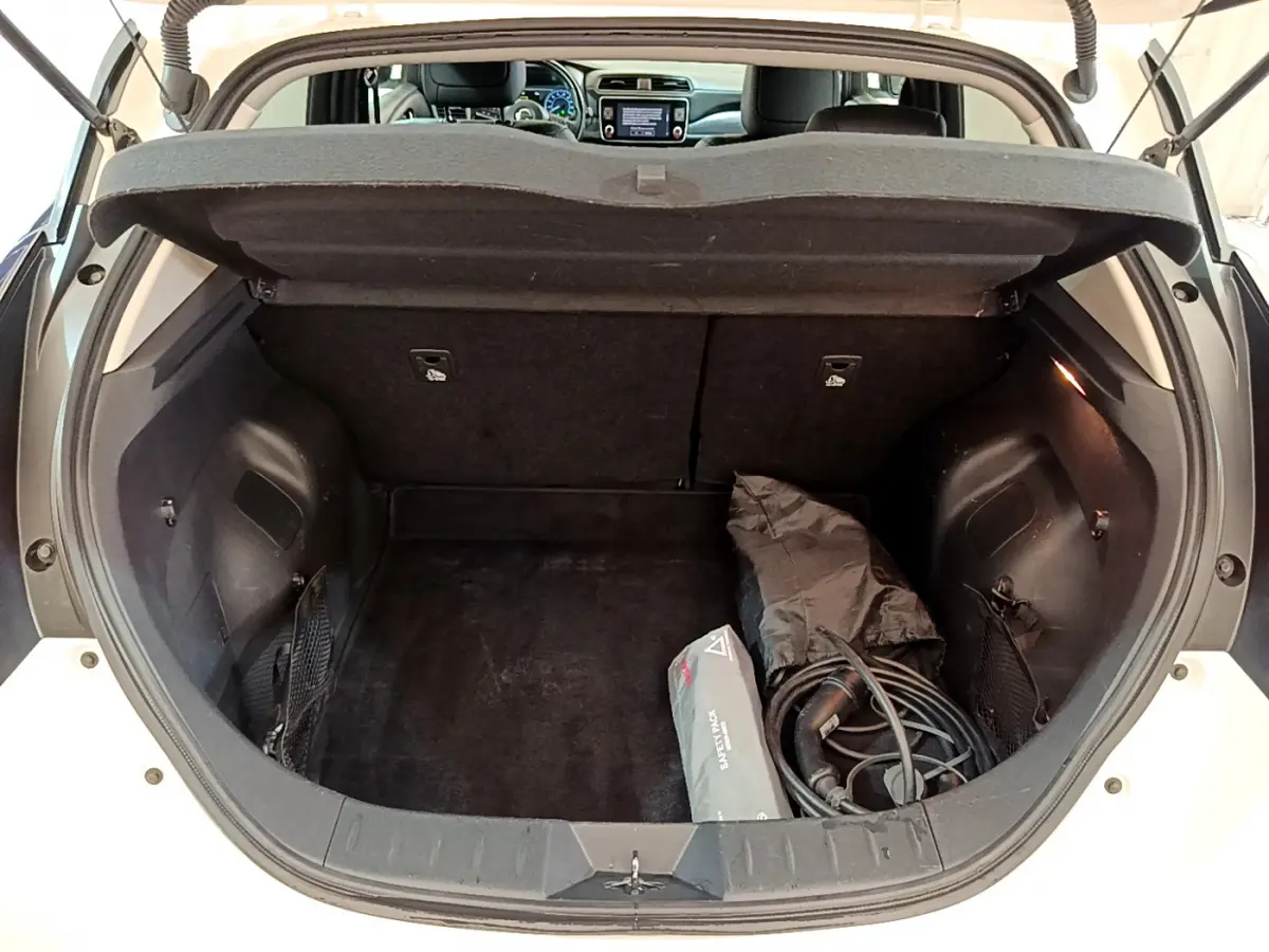 Coffre ouvert vue arrière d'une Nissan Leaf blanche 2020, avec câbles de recharge et trousse de secours visibles.