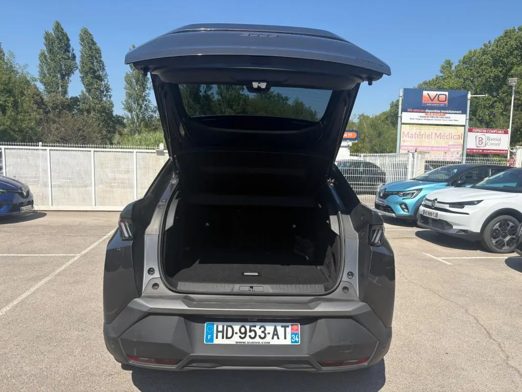 Vue arrière d’un Peugeot 3008 Hybrid gris 2025 avec coffre ouvert sur parking ensoleillé.
