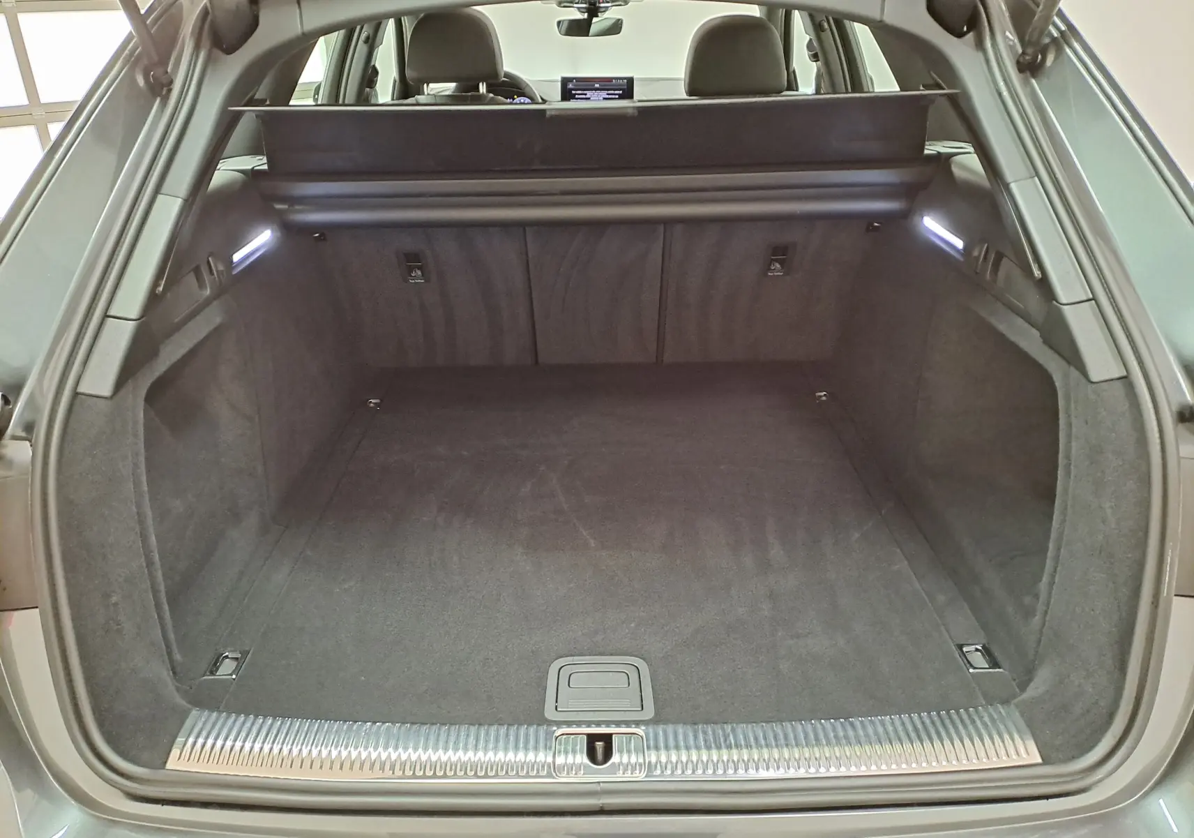 Coffre ouvert de l'Audi A4 Avant 40 TDI gris Daytona, vue arrière montrant l'espace de chargement et la finition intérieure noire.