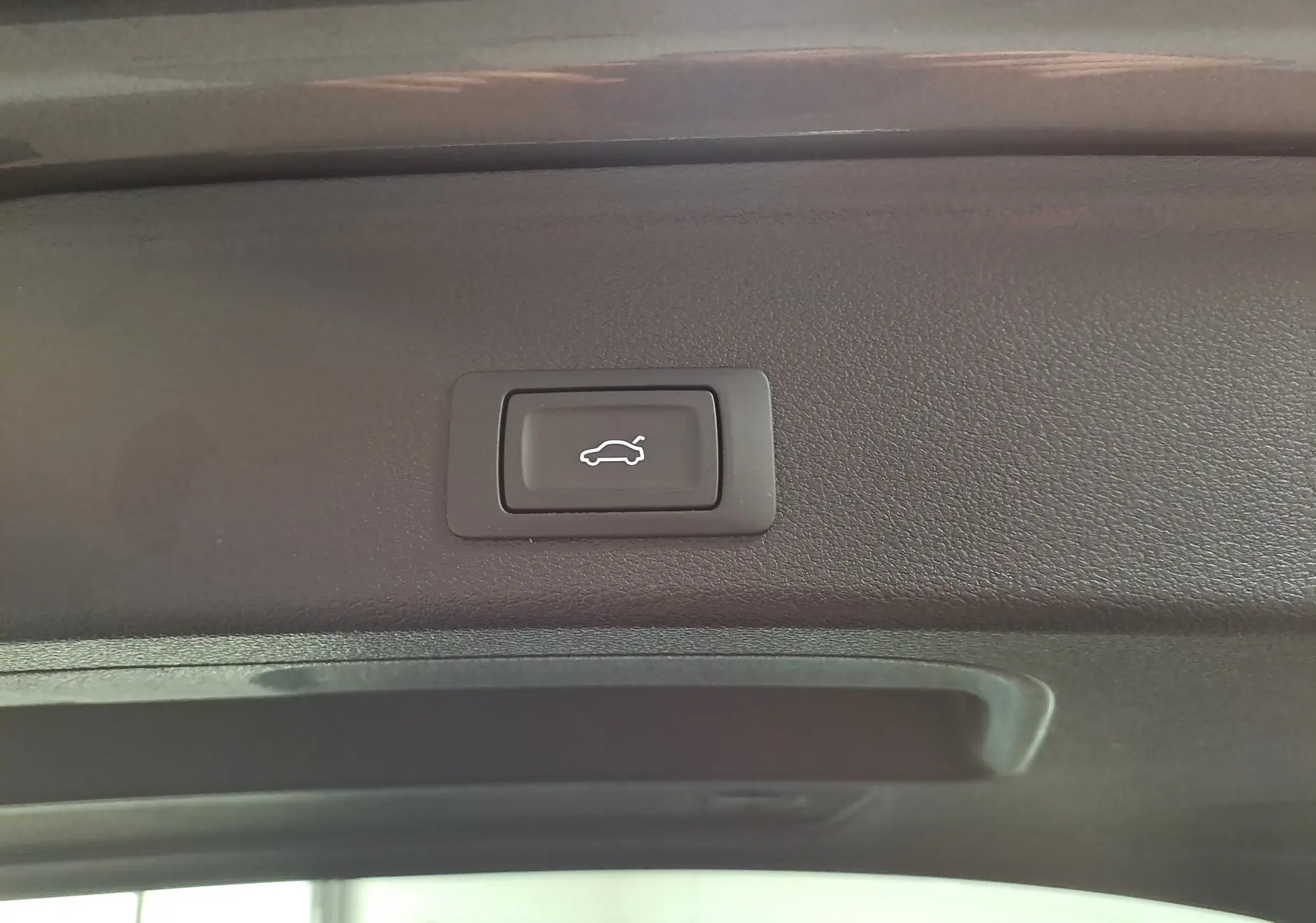 Bouton d'ouverture électrique du hayon sur le bord intérieur du coffre d'une Audi A4 Avant Gris Daytona 2024.