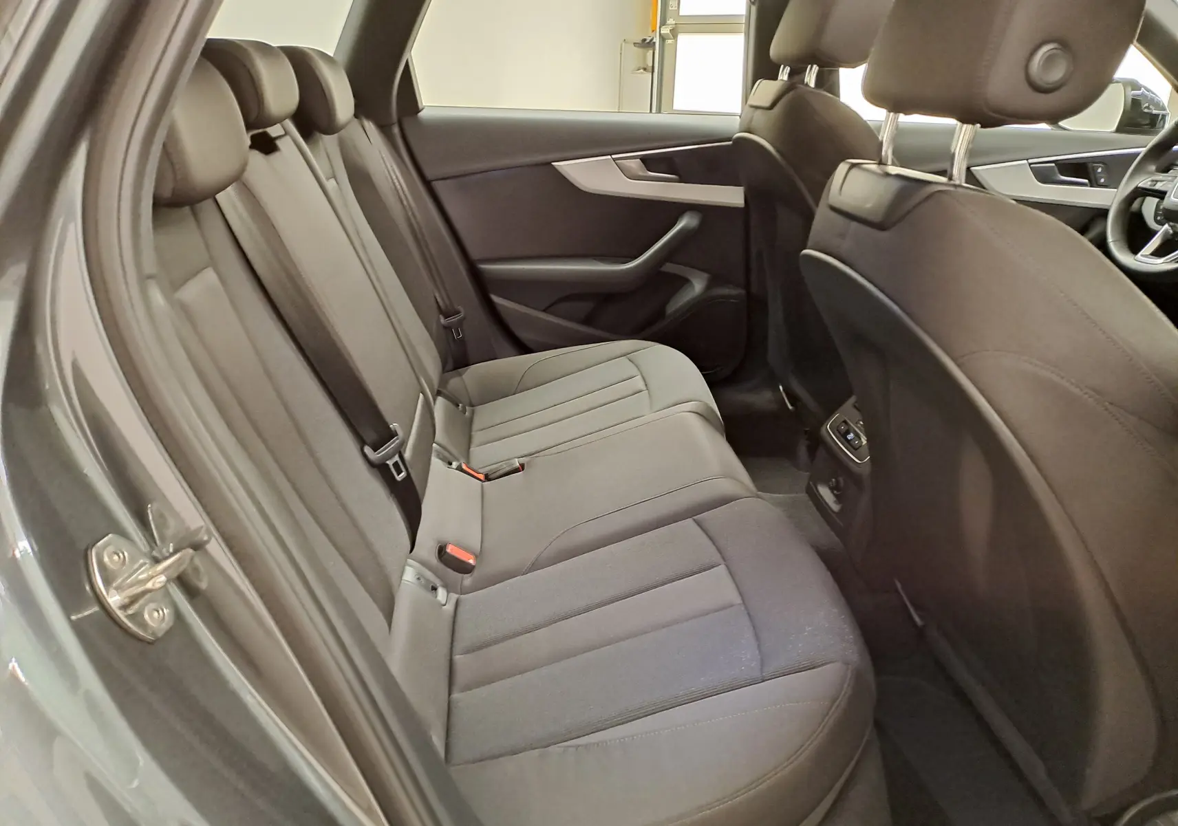 Vue intérieure côté gauche des sièges arrière en tissu gris d'une Audi A4 Avant 40 TDI 2024 avec portes ouvertes.
