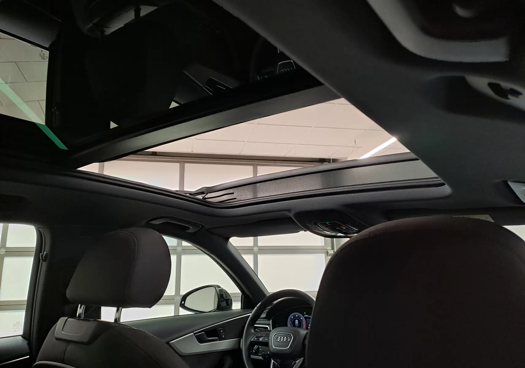 Vue intérieure de l'Audi A4 Avant 2024 avec toit panoramique ouvert et sièges avant noirs.