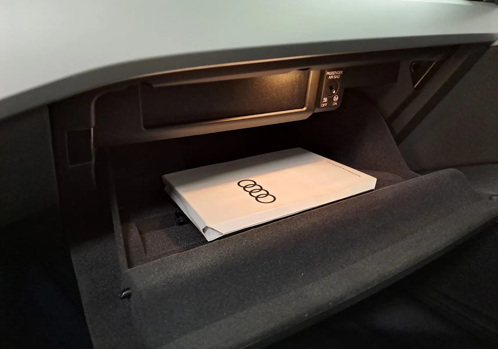 Gros plan sur la boîte à gants ouverte de l'Audi A4 Avant 40 TDI 2024 avec manuel et éclairage intérieur.