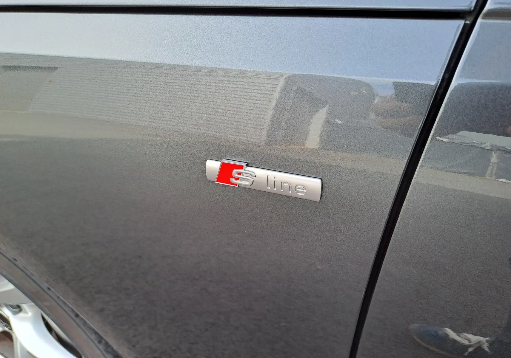Gros plan sur l'emblème S line sur la porte côté gauche d'une Audi A4 Avant 2024 gris Daytona métallisé.