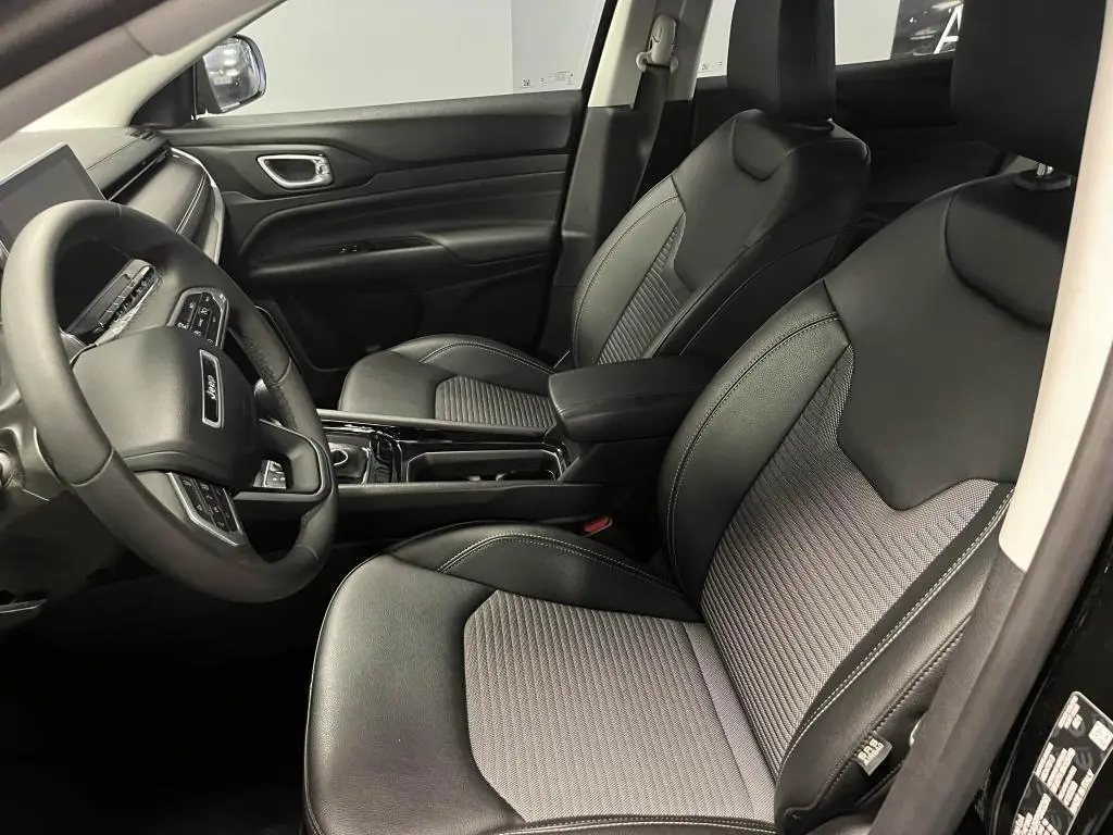 Intérieur avant du Jeep Compass 2024, sièges mixte noir et gris, volant multifonctions et console centrale brillante.
