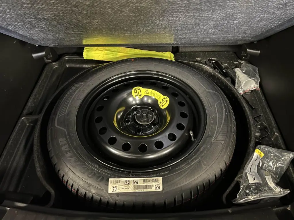 Roue de secours temporaire noire dans le coffre du Jeep Compass 2024, version hybride essence Altitude.