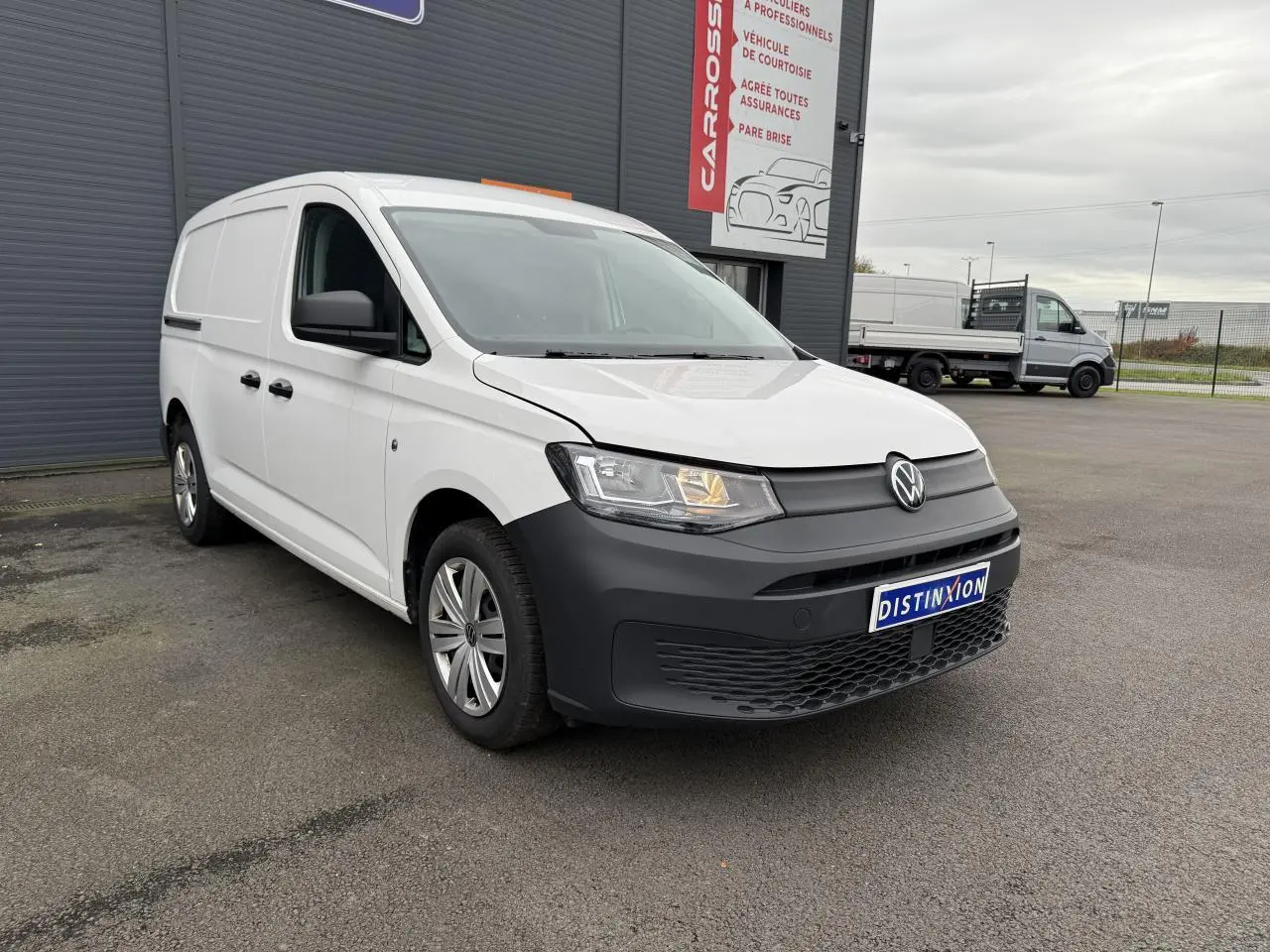 Volkswagen Caddy Maxi Cargo blanc candy vu en 3/4 avant droit avec pare-chocs noir mat et feux allumés.