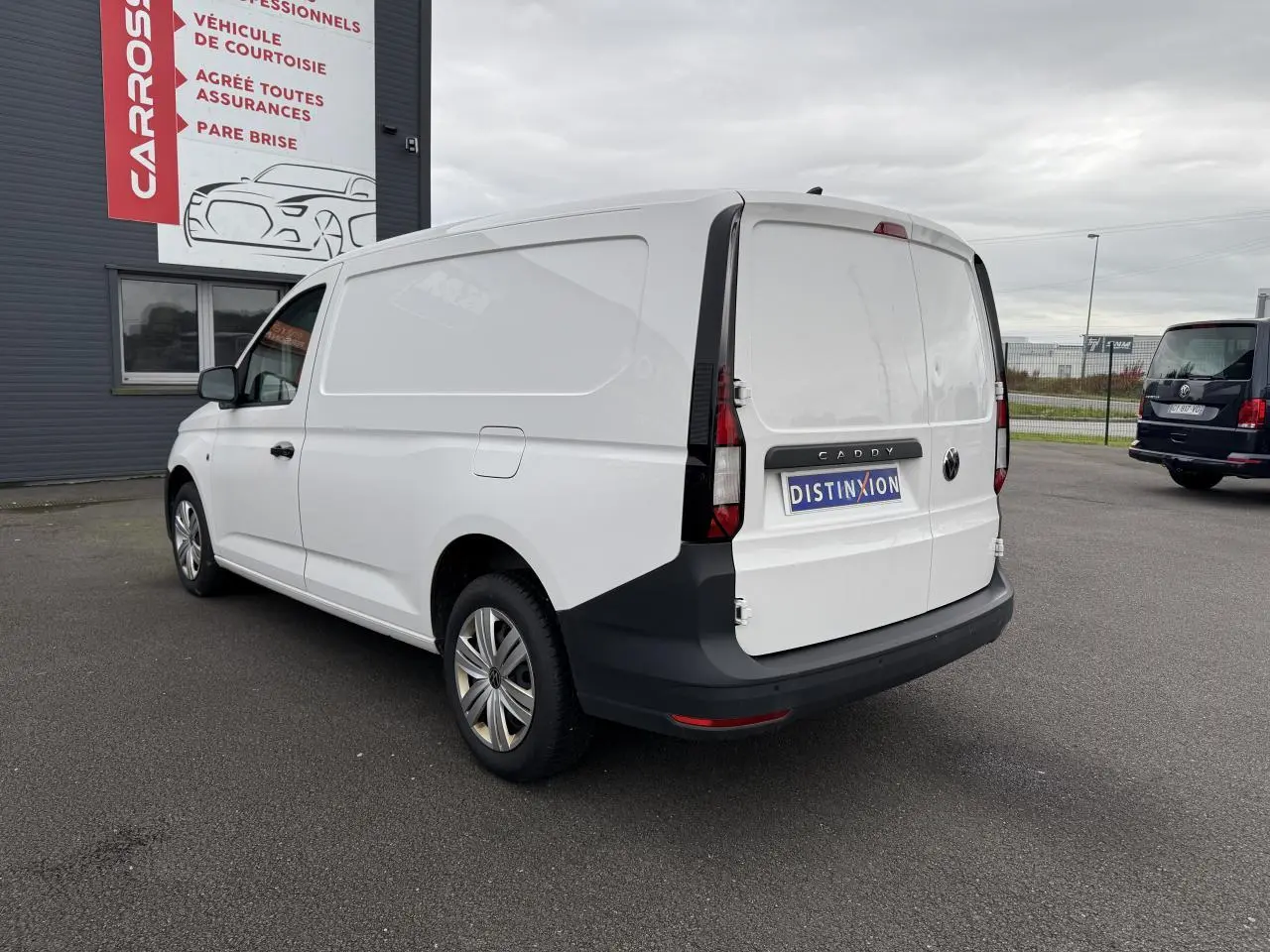 Vue 3/4 arrière droite d’un Volkswagen Caddy Maxi Cargo blanc Candy avec pare-chocs noirs et porte coulissante visible.
