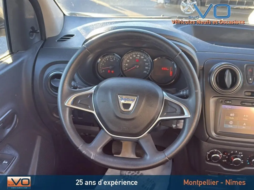 Vue centrée sur le volant et le tableau de bord noir du Dacia Lodgy blanc, avec commandes et écran tactile visibles.