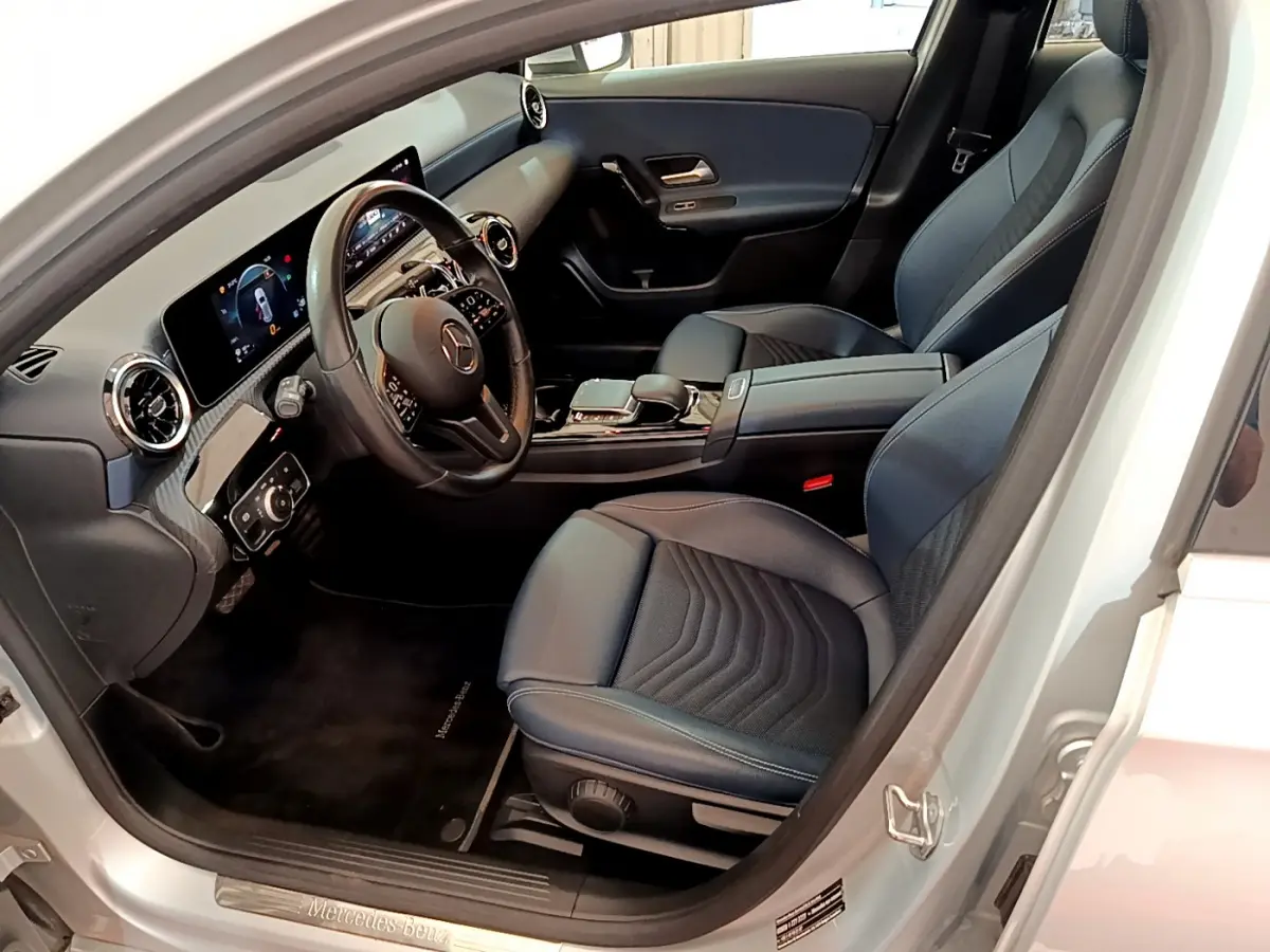 Intérieur côté conducteur d'une Mercedes Classe A gris clair, avec tableau de bord numérique et sièges en cuir noir.