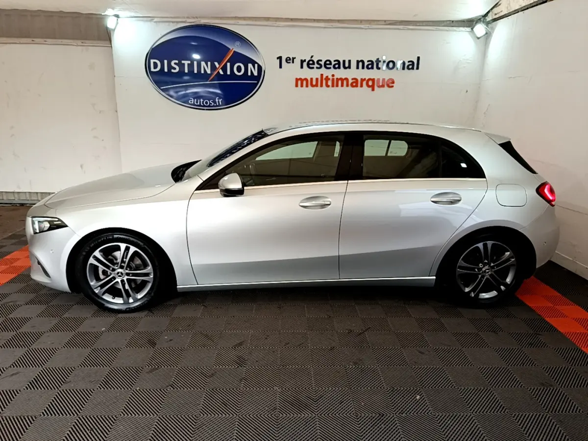 Profil côté gauche d'une Mercedes Classe A gris clair 2020 garée en intérieur sur sol à damier noir et orange.