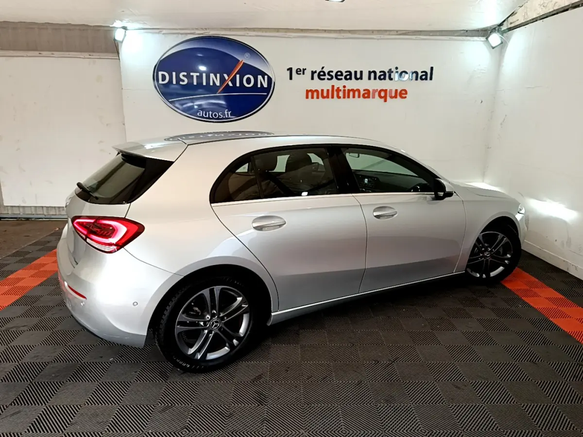 Vue 3/4 arrière droite d'une Mercedes Classe A A 180 d Business Line gris clair dans un showroom multimarque.