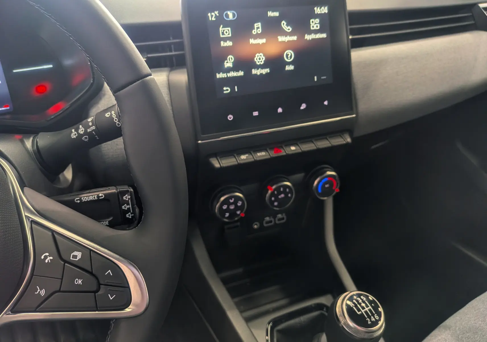 Vue intérieure centrée sur la console centrale et levier de vitesse manuelle d'une Renault Clio V gris schiste, avec écran tactile allumé.
