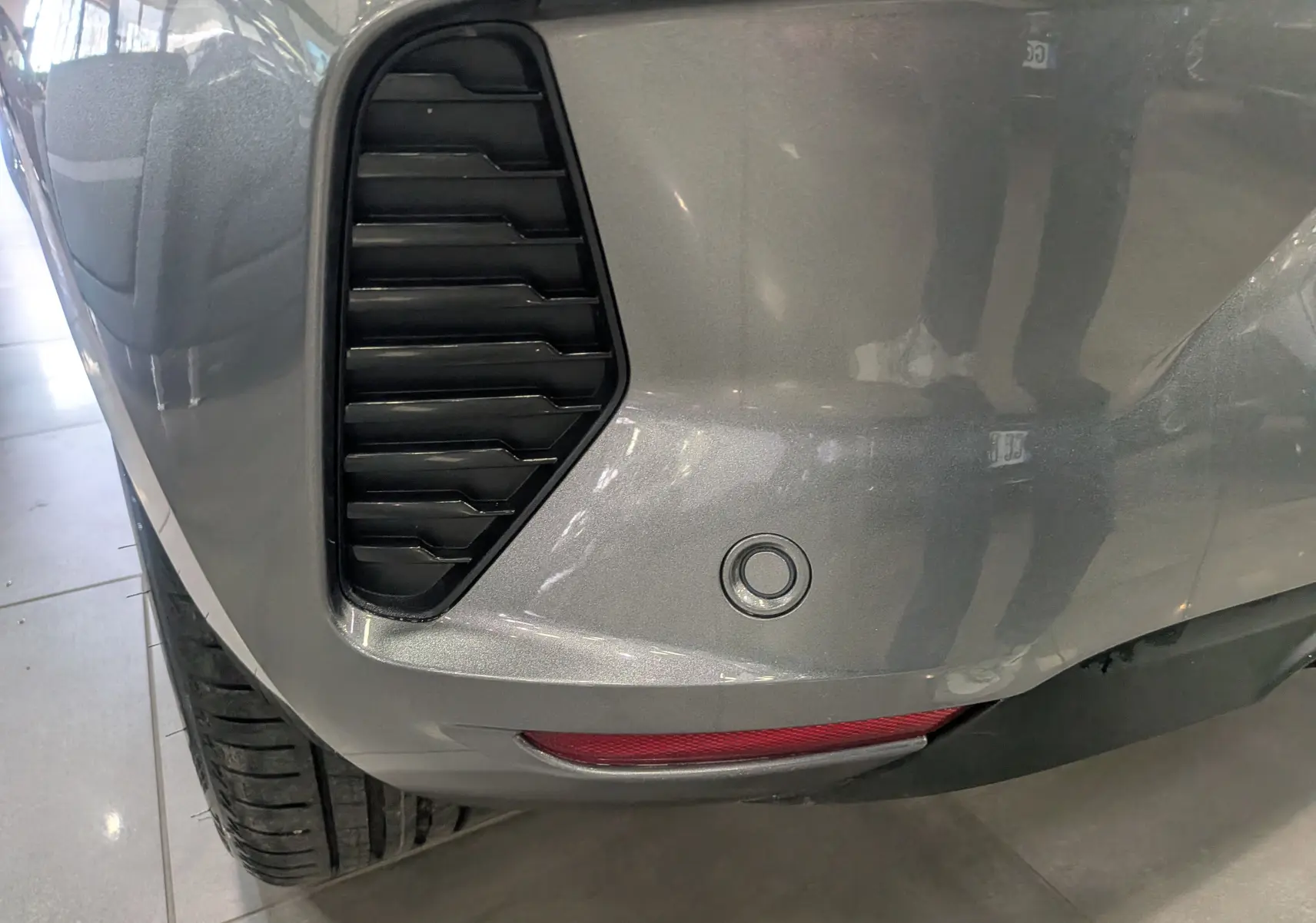 Gros plan sur le pare-chocs arrière droit gris schiste d'une Renault Clio V 2025 avec capteur de recul et diffuseur noir.