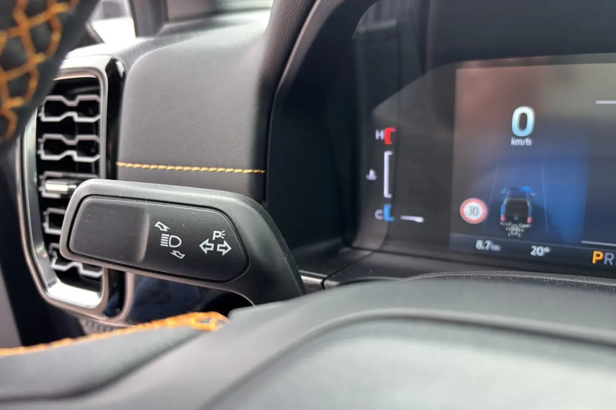 Gros plan sur le commodo gauche et le tableau de bord numérique du Ford Ranger noir agate, avec surpiqûres orange visibles.