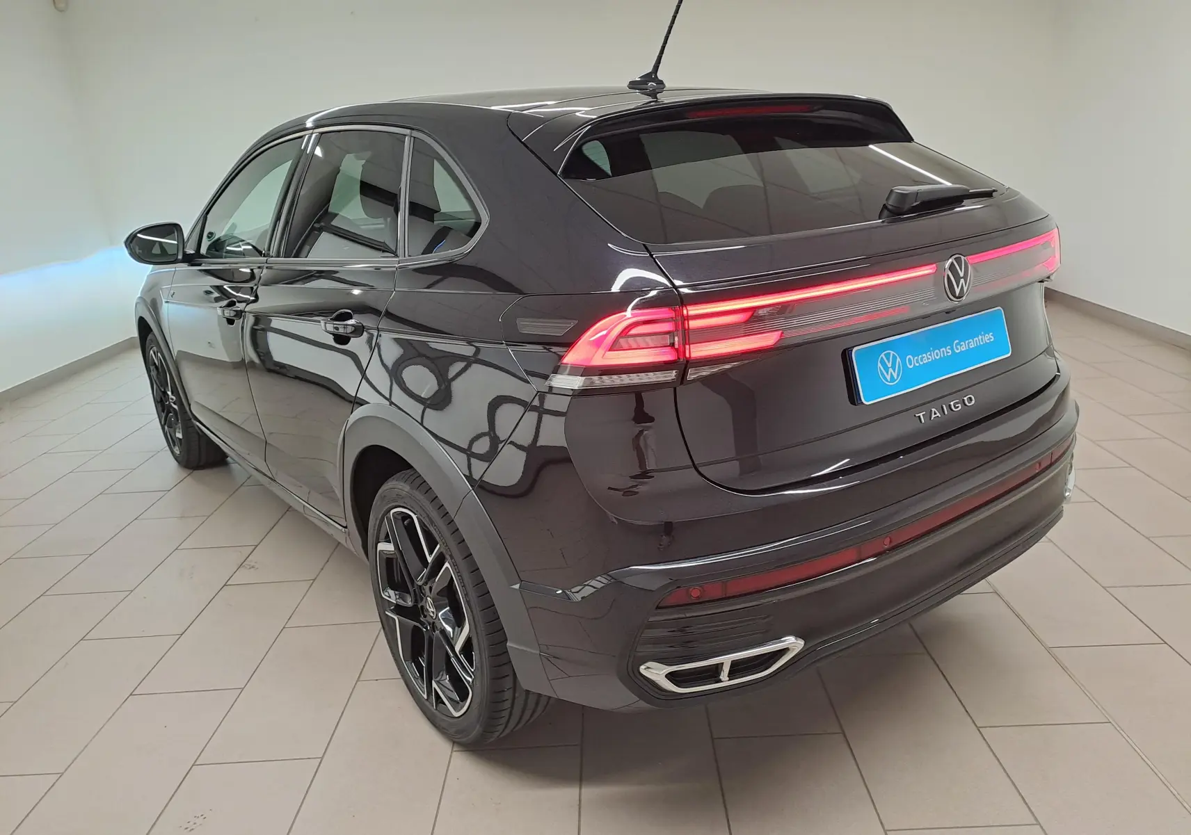 Vue 3/4 arrière droite du Volkswagen Taigo noir intense nacré avec feux arrière LED et jantes alliage noires R-Line.