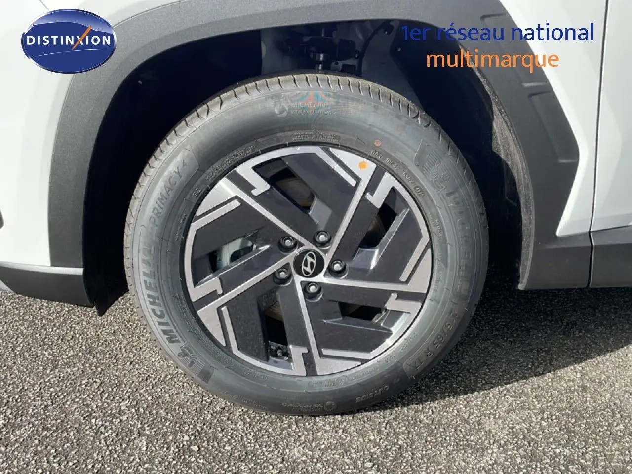 Gros plan sur la roue avant droite du Hyundai Tucson blanc Atlas, avec jante alliage noire et grise au design géométrique.