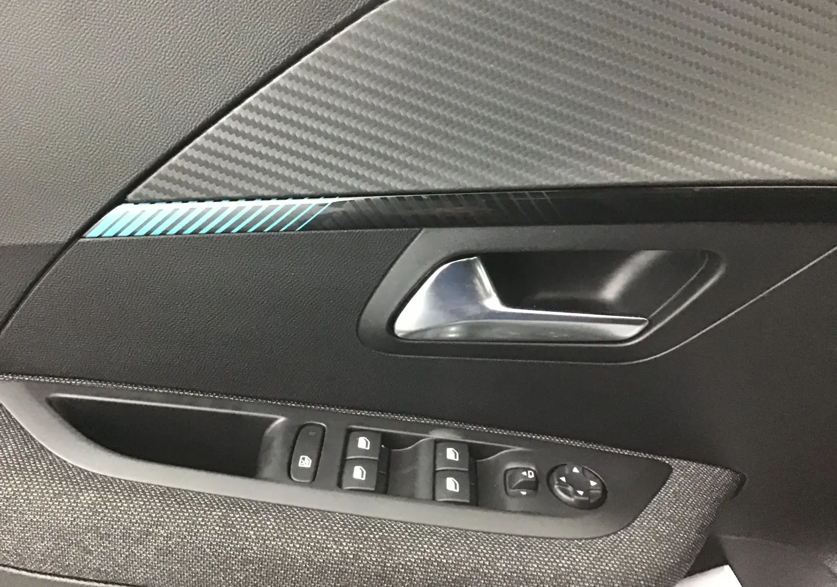 Poignée intérieure côté gauche de la Peugeot 208 gris Artense avec commandes de vitres et décor carbone bleu.